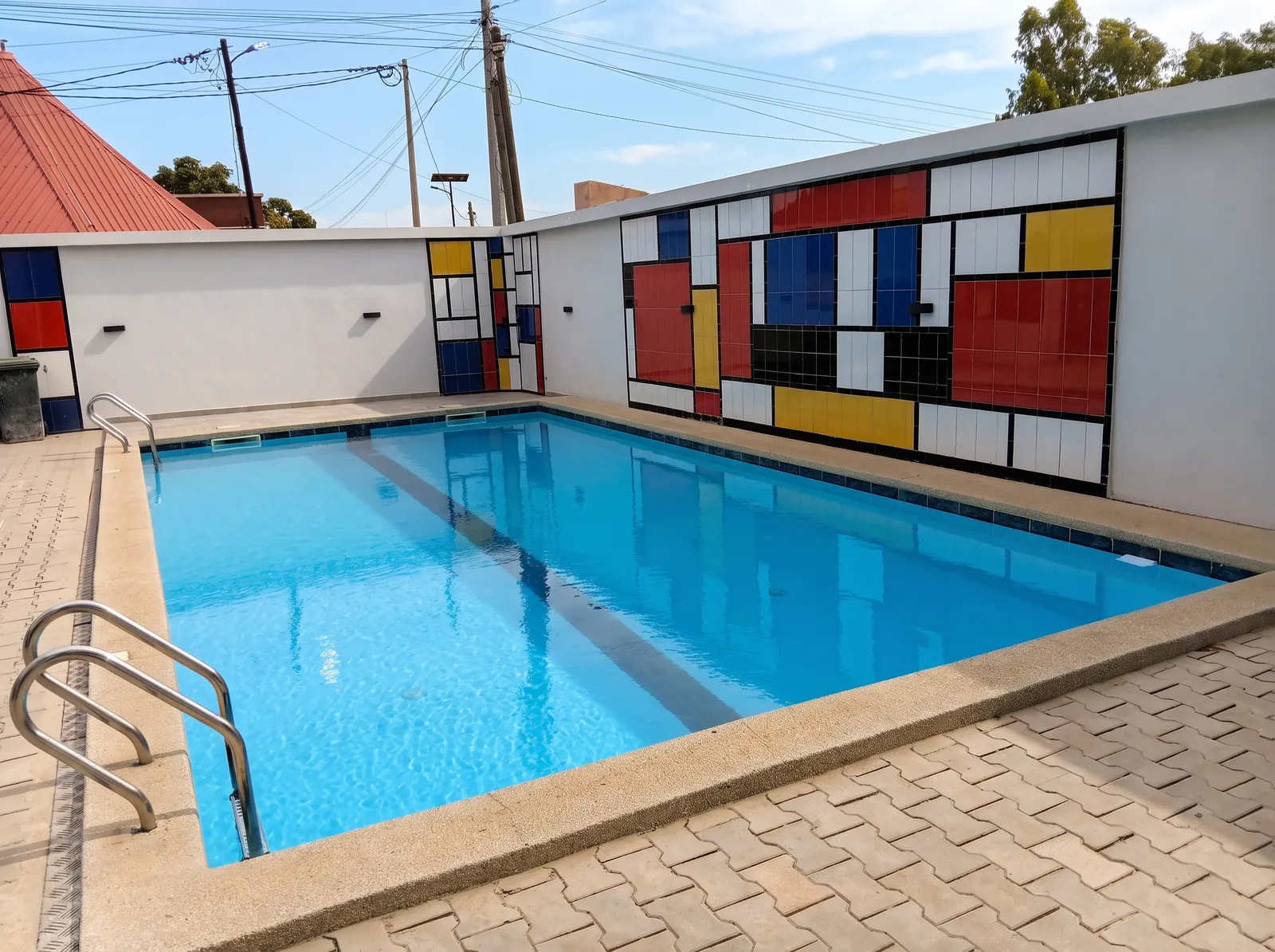 Piscine extérieure du Mondrian bordée d'une terrasse pavée, face à un mur décoré de carreaux blancs, rouges, bleus et jaunes.