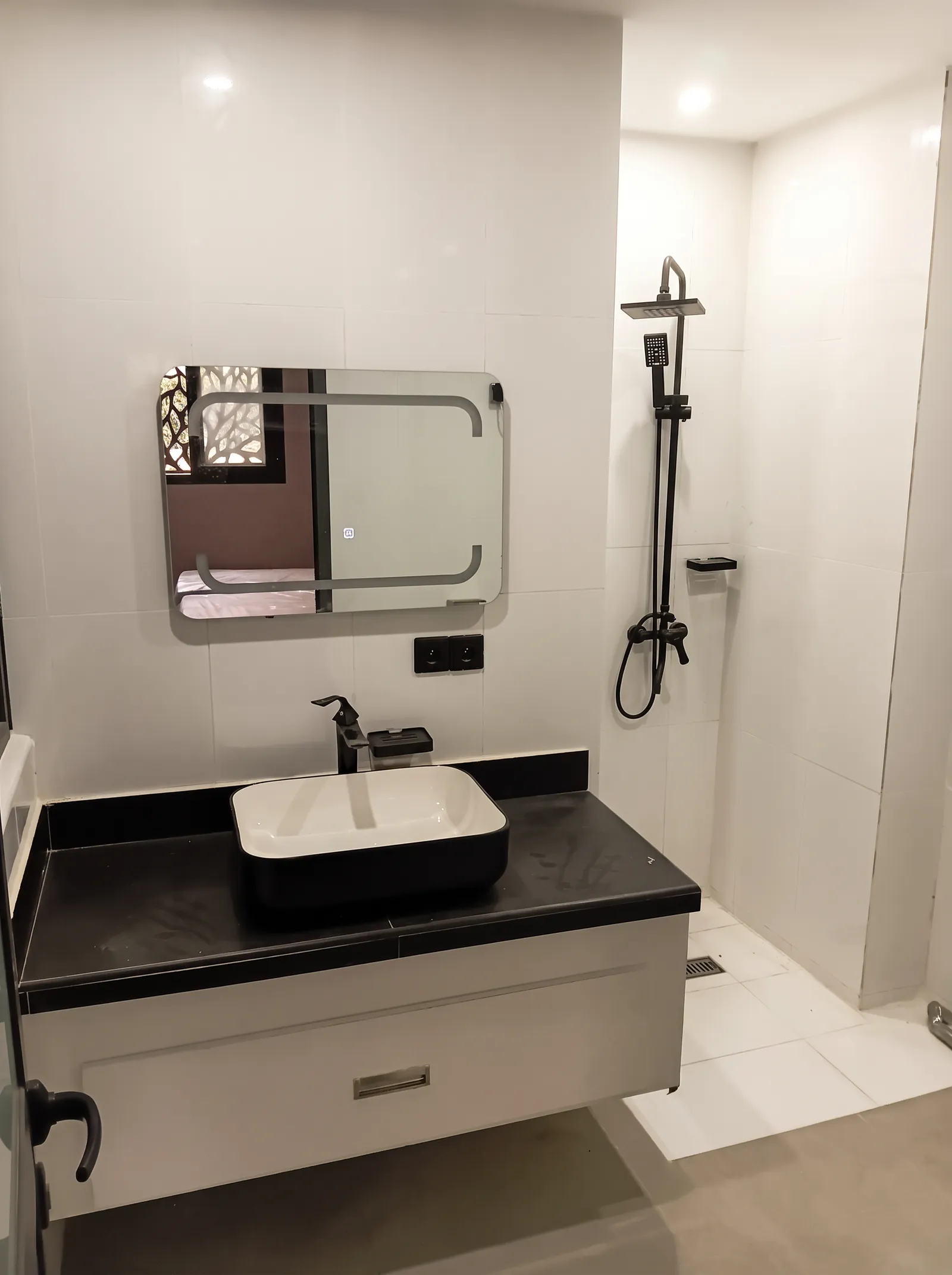 Salle de bain avec vasque sur plan de travail noir, miroir et douche à l'italienne.